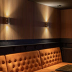 Lamellenwand met wandlampen boven een zitbank.