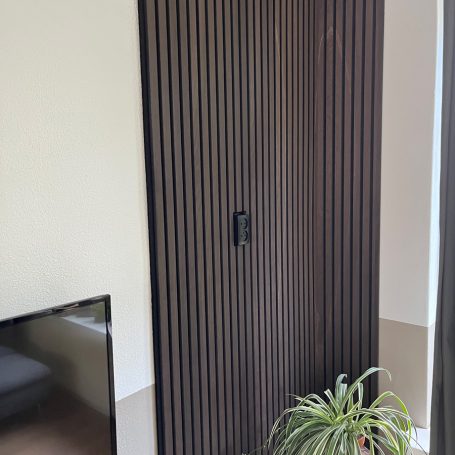 Donkere lamellenwand naast een televisie en plant.