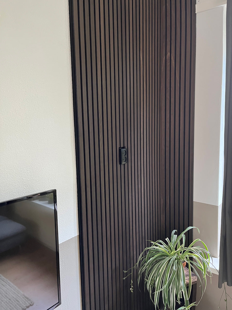Donkere lamellenwand naast een televisie en plant.