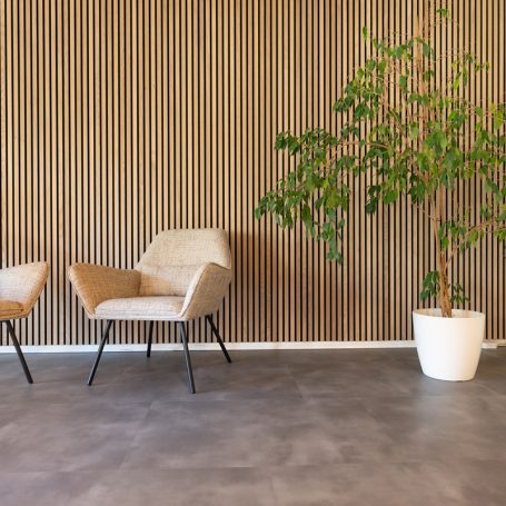 Lamellenwand achter twee stoelen en een grote plant in een witte pot.