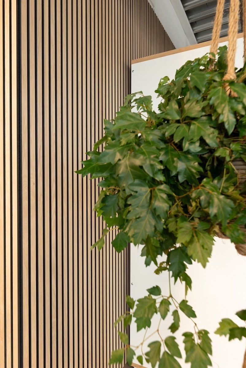 Detail van een lamellenwand naast groene bladeren.