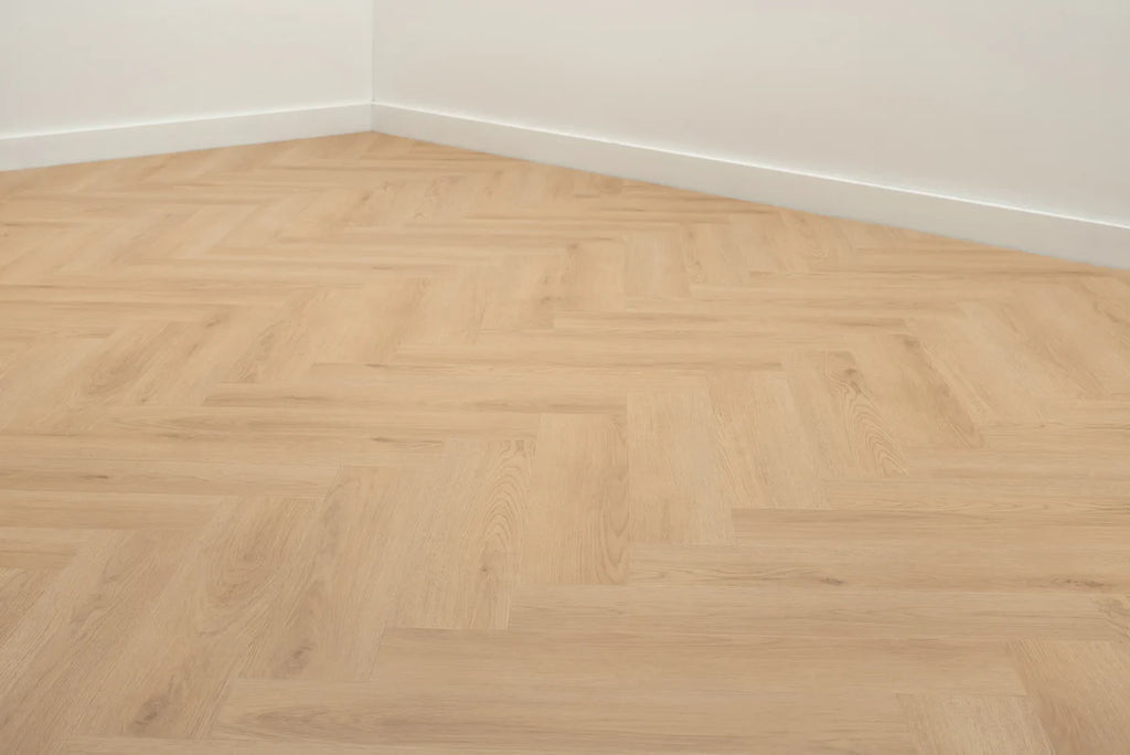 Lichte visgraatvloer in een kamer met witte plinten.