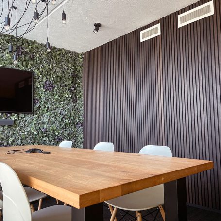 Donkere lamellenwand achter een eettafel met lichte stoelen.