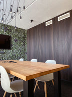 Donkere lamellenwand achter een eettafel met lichte stoelen.