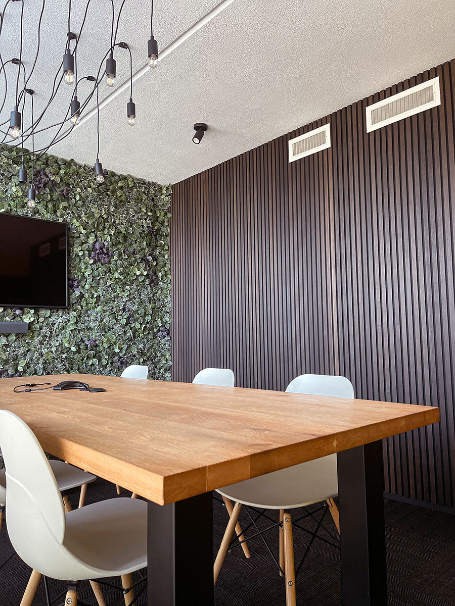 Donkere lamellenwand achter een eettafel met lichte stoelen.