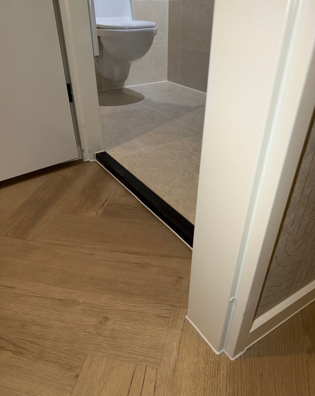 Afgewerkte vloer bij de toiletdeur en donkere dorpel