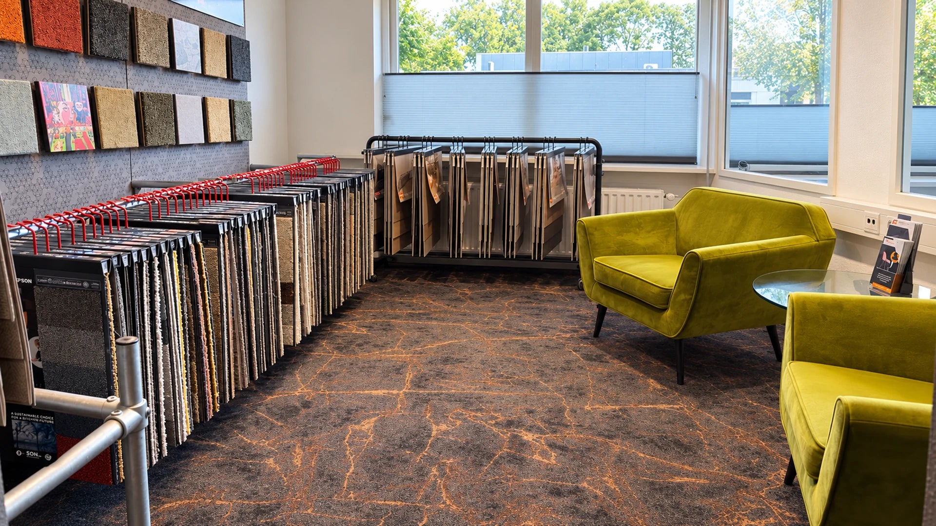 Tapijtstalen en twee groene stoelen in de tapijthoek van de showroom